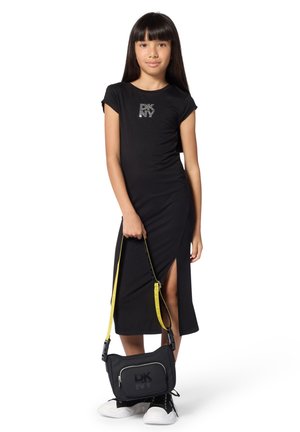 Robe midi noire à manches courtes avec fentes latérales et logo en strass, associée à un sac bandoulière noir avec une sangle jaune et un marquage audacieux.