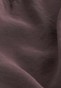 Tissu doux et texturé dans un mauve profond, présentant un léger éclat et de douces ondulations, créant un aspect fluide et drapé.