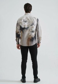 Chemise à manches longues ornée de grands motifs floraux dans des couleurs douces, avec un tissu lisse et une fermeture à boutons, portée sur un jean skinny noir.