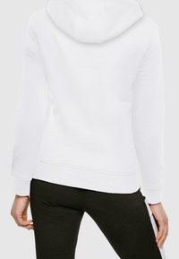 Biała bluza z kapturem o miękkim wykończeniu, posiadająca kaptur, ściągacze na rękawach i prosty dolny brzeg. W połączeniu z czarnymi legginsami sportowymi.