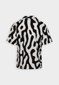 Camicia a maniche corte in bianco e nero con un motivo astratto ondulato. Presenta un colletto e una vestibilità ampia, realizzata in un tessuto morbido.