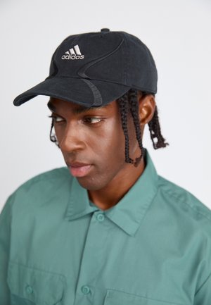 Sort Adidas-kasket med buet skygge og broderet logo; båret med en grøn knap-ned skjorte med krave og to forlommer.