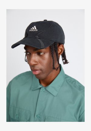 Zwarte Adidas pet met een gebogen rand en geborduurd logo; gedragen met een groene button-up shirt met kraag en twee voorzakken.