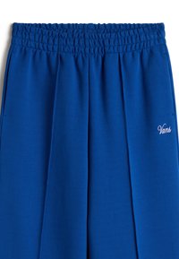 Pantalones de chándal azul con cinturilla elástica y diseño plisado. Presenta un pequeño logo "Vans" rosa en la parte inferior de la pierna. Textura suave y lisa.