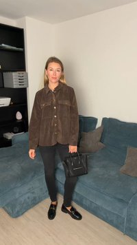 Brun fløjlsnappet skjorte med to brystlommer, båret med sorte bukser og sorte loafers. Holder en lille sort håndtaske.