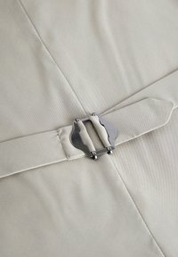 Beige színű szövet, sima textúrával, ezüst színű fémetalapú csattal és letisztult vonalakkal. A design a egyszerű, funkcionális elemeket hangsúlyozza.