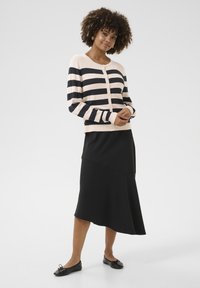 Striped cardigan in beige and navy, with long sleeves and button closure, paired with a black asymmetrical skirt and black ballet flats.