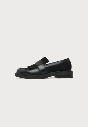 Mocassin en cuir noir avec un petit talon et des empiècements en daim, avec une large bride sur le dessus et un bout arrondi.