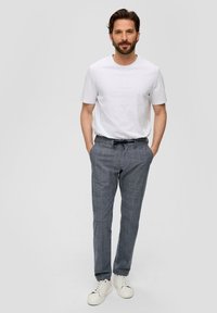 Grijze geruite broek met een trekkoord in de taille, gecombineerd met een eenvoudig wit t-shirt en witte sneakers. Casual pasvorm, zachte stof.
