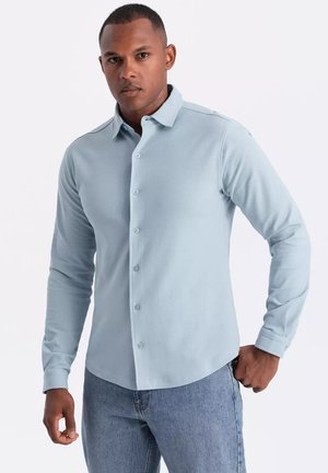 Camisa de manga larga de color azul claro con un diseño de botones, textura de tela suave y cuello puntiagudo, combinada con unos jeans de mezclilla.