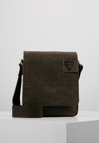 Borsa a tracolla in pelle marrone con chiusura a pattina, tracolla regolabile e un'etichetta decorativa del marchio. Presenta dettagli di cucitura.
