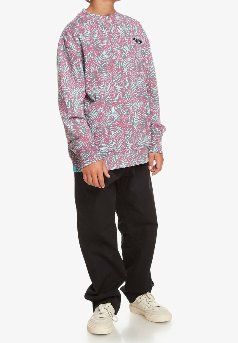 Felpa a maniche lunghe con un motivo astratto rosa, verde acqua e bianco, con scollo rotondo e vestibilità rilassata, abbinata a pantaloni neri.