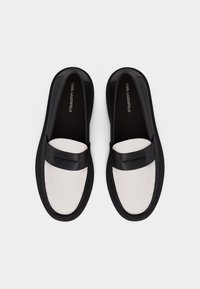 Μαύρα και λευκά μοκασίνια Karl Lagerfeld με μαύρο λουράκι και το όνομα της μάρκας στο πάνω μέρος, απεικονιζόμενα από ψηλά σε λευκό φόντο.