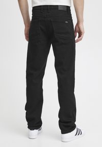 Pantalones vaqueros de mezclilla negra con corte recto, que cuentan con dos bolsillos traseros y una cinturilla texturizada, llevados con zapatillas blancas.