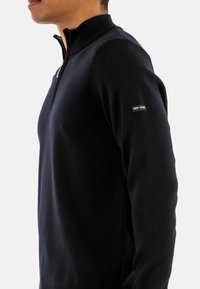Maglione navy a girocollo con mezzo zip, polsini a coste e una piccola etichetta sulla manica sinistra. Realizzato in morbido tessuto a maglia.