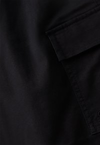 Černá látka s hladkým povrchem, vybavená boční kapsou a viditelnými švy. Jednoduchý design bez vzorů nebo ozdob.