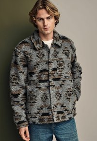 Fleece jacket in gray with brown and black patterns, featuring a collared neckline, front pockets, and a soft, textured appearance.