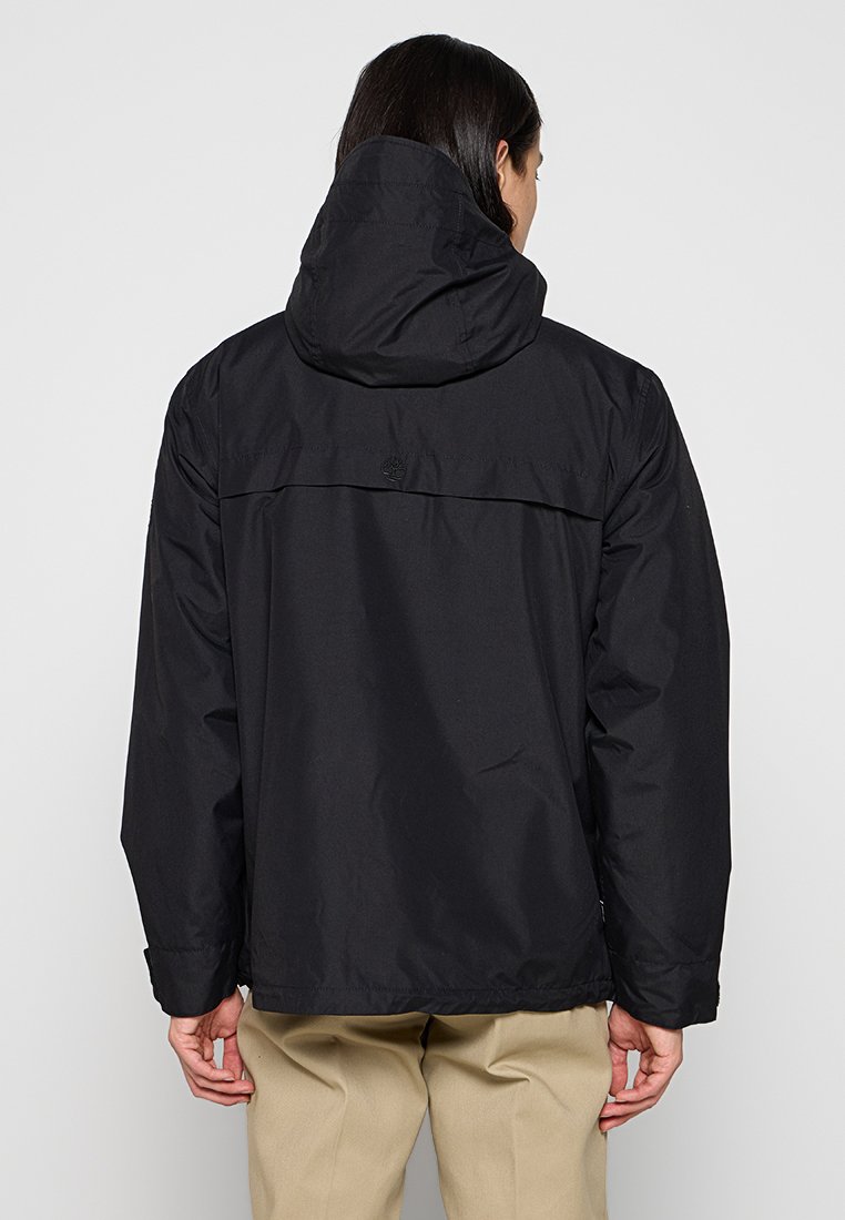 Chaqueta negra impermeable con capucha, con un corte recto, textura suave y diseño minimalista. Incluye un detalle del logotipo en la parte trasera.