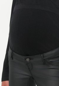 Pantalones de maternidad negros con una tela suave y elástica, que cuentan con un cierre de botón etiquetado como "SOLO" y una amplia cinturilla elástica.