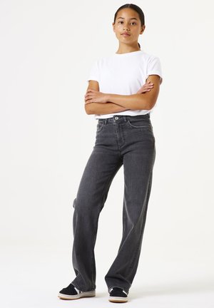 Jeans neri a vita alta, fit dritto, con cinque tasche e cuciture in evidenza. Abbinati a una t-shirt bianca a maniche corte e sneakers nere.