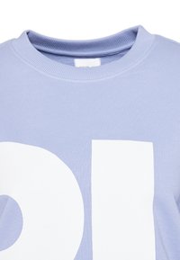 Pull bleu clair col rond avec de grandes lettres blanches en bloc partiellement visibles sur le devant.
