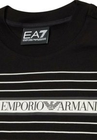 Maglietta nera con strisce bianche orizzontali e un'etichetta centrale con il logo "EMPORIO ARMANI" e un emblema di aquila sopra di essa.