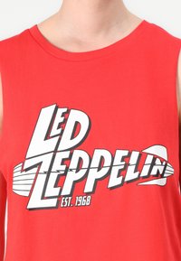 Red cotton sleeveless shirt featuring large white and black "LED ZEPPELIN" graphic with lightning bolt and "EST. 1968" text at the bottom.