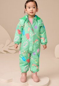 Groene gewatteerde sneeuwpak met abstracte, veelkleurige patronen. Heeft een capuchon, een rits aan de voorkant en elastische manchetten. Gecombineerd met roze rubberen laarzen.