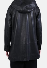 Chaqueta de cuero negra con capucha, presenta un ajuste ligeramente holgado, textura suave y detalles de costuras en la parte trasera y las mangas.