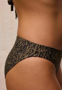 Bikini-Unterteil in Olivgrün mit einem schwarzen abstrakten Muster. Hochgeschnittener Schnitt mit glattem Stoff und sauberen Nähten.