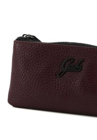 Borsa in pelle bordeaux con finitura testurizzata, dotata di una cerniera nera e un logo nero in rilievo sul lato. Forma compatta e rettangolare.