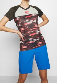 Tričko na cvičení má multicolorovaný, strukturovaný síťovaný design s krátkými rukávy, v kombinaci s modrými šortkami, které mají boční kapsy.