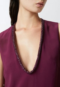 Blusa con scollo a V profondo in ricco tessuto bordeaux, caratterizzata da un colletto decorato con perline testurizzate. Tessuto morbido, design senza maniche.