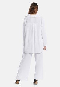Witte katoenen loungewear set met een losse lange mouwen blouse met kraag en brede broekspijpen. Zacht, gestructureerd materiaal met minimale details.