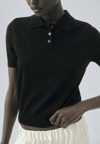 Černé polo tričko s krátkým rukávem vyrobené z měkkého materiálu, s klasickým límečkem a třemi knoflíky. Hladká textura, těsný střih.