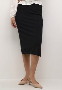 Schwarzer Strickbleistiftrock mit mittellanger Passform, der einen schlichten Saum hat. Kombiniert mit nudefarbenen Slingback-Absatzschuhen.