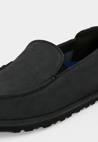 Μαύρο σουέντ παπούτσι τύπου slip-on με ραφές μοκασίνου και λαστιχένια σόλα, σε γωνιακή κοντινή λήψη που δείχνει το πάνω μέρος και το πλάι.