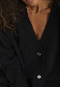 Black cardigan made of soft fabric, featuring a deep V-neck, textured surface, and two decorative buttons in contrasting colors.