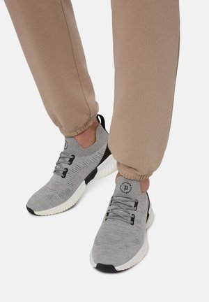 Sneakers atletici grigi con tomaia testurizzata, lacci elastici e suola bianca ammortizzata. Abbinati a pantaloni jogger color panna.
