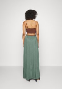 Bruine cropped top met dunne bandjes, gecombineerd met een lange, vloeiende groene rok, voorzien van een elastische tailleband en een riemaccent.