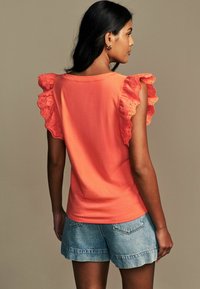 T-shirt di cotone corallo con maniche in pizzo scallop, vestibilità rilassata, abbinato a pantaloni corti di denim azzurro, mostrato da una vista posteriore.