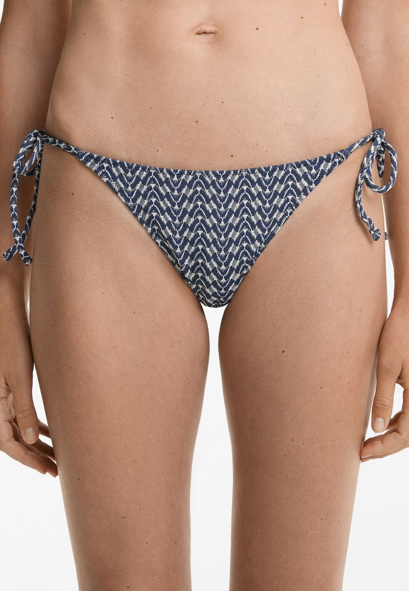 Námořnická modrá a bílá vzorovaná bikinová spodní část s vázacími uzávěry na bocích. Má geometrický design a nízký pas, vyrobená z elastické plavecké tkaniny.