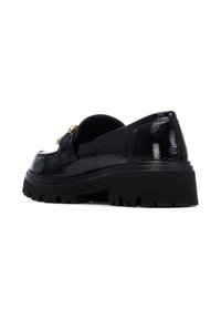 Mocasines de charol negro con suela gruesa, que presentan herrajes en tono dorado y un acabado texturizado. La vista lateral muestra la forma redondeada.