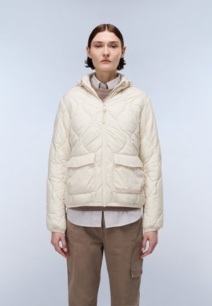 Lichtbeige gewatteerde jas met een capuchon, rits aan de voorkant, twee voorzakken, elastische manchetten, gedragen over een beige coltrui en een gestreept shirt.