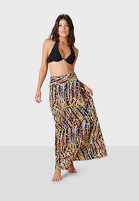 Mustat halterneck-bikinitoppit yhdistettynä värikkään, kuvioidun maksihameen kanssa, jossa on abstrakteja raitoja ja leveä vyötärönauha.