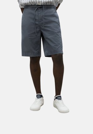 Pantalones cortos grises con una cintura elástica y cordón, que presentan bolsillos laterales y un corte relajado. Combinados con zapatillas blancas.