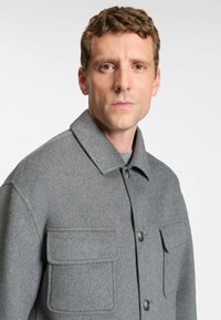 Grå uldjakke med krave, to forlommer og knaplukning. Stoffet har et blødt, struktureret udseende.