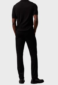 Zwarte poloshirt met korte mouwen, gecombineerd met nauwsluitende zwarte broek en glanzende zwarte schoenen, met een gladde textuur en een eenvoudig ontwerp.