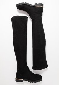 Botas negras, por encima de la rodilla, hechas de suave gamuza, con una suela plana que cuenta con un agarre de goma texturizado y un diseño ajustado y elegante.