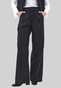 Zwarte pantalon met krijtstreep, gemaakt van een gestructureerde stof, met een hoge taille, brede pijpen en zijzakken, gecombineerd met zwart schoeisel.